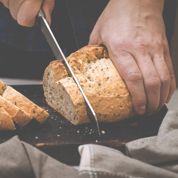 Pâtisseries maison. Les mains des hommes coupent du pain rougissant fait maison dans la cuisine
 - Photo, image