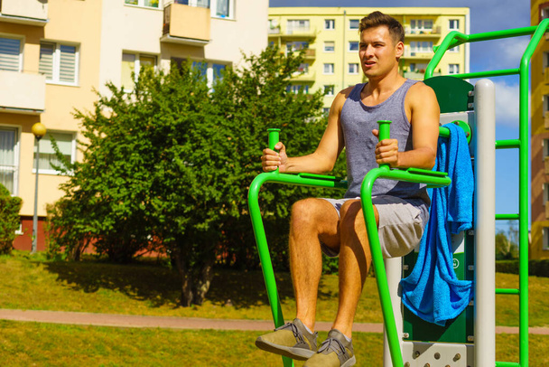 Young handsome man working out in outdoor gym. Sporty guy flexing his muscles doing sit ups on machine. Staying fit and healthy. - Фото, изображение