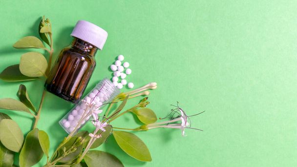 散在するホメオパシー薬と緑の背景に葉を持つガラス瓶 - 写真・画像