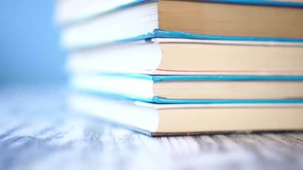 Corner of a stack of multi-colored books in hard and soft cover on a blue bright background. On a wooden old table. Close-up. Camera moves up - Footage, Video