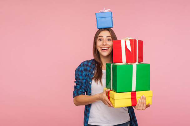 Portrait of pretty girl looking at camera with expression of sincere childhood happiness and holding many gifts, one box on head, enjoying birthday presents, christmas holidays. studio shot isolated - Photo, Image