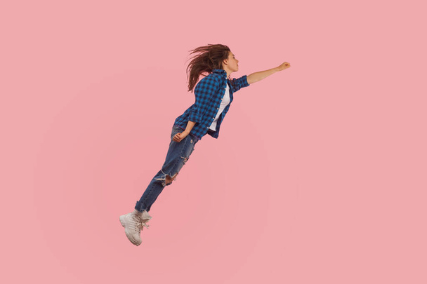 Portrait of girl in casual style outfit flying up in air with raised fist, moving forward to victories, feeling freedom, power and confidence to achieve goal. studio shot isolated on pink background - Fotó, kép