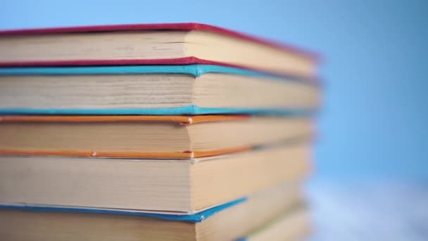 stack of colorful hardback books on a blue bright background. On a wooden old table. Close-up. The camera moves down - Πλάνα, βίντεο