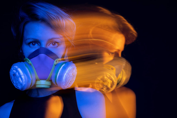 respirator mask young woman portrait. black background. Covid virus corona environmental disaster polluted air. Blue and orange. Dramatic emotional look eyes. Looking side profile. Protection tool - Photo, Image