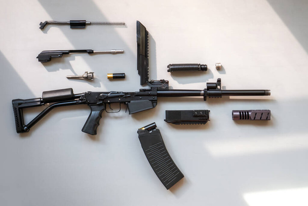 Disassembled machine gun on a gray background. Isolated. Details of firearms in a disassembled state. Light falls from the window and creates shadows . - Photo, image