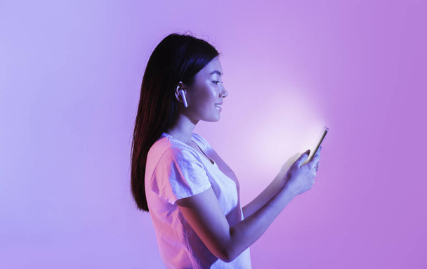 Woman with wireless headphones look at glowing smartphone - Fotografie, Obrázek