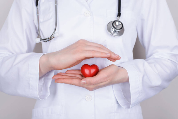 Vitality healthy lifestyle concept. Cropped close up photo of nurse making a roof over little small heart in her hands isolated over grey background - Photo, Image