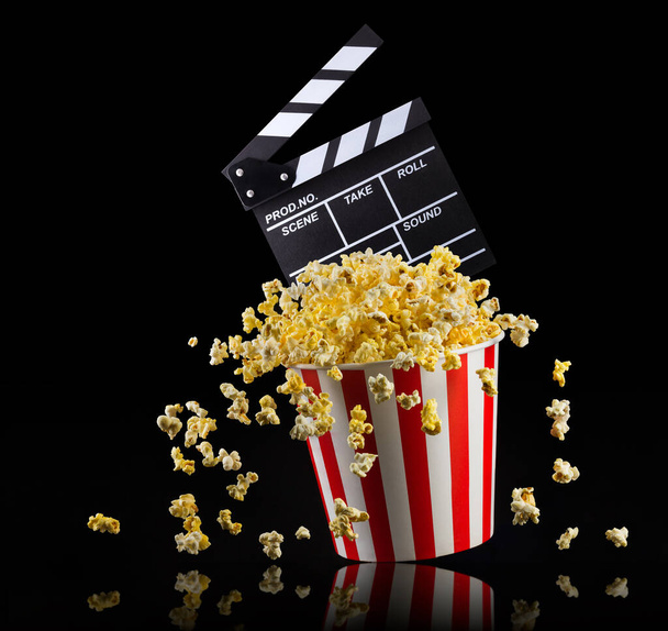 Flying popcorn and film clapper board isolated on black background - Foto, imagen