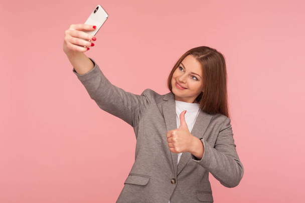 Takım elbiseli iyimser bir iş kadınının portresi başparmak hareketleriyle video görüşmesi yapıyor, cep telefonu, kurumsal cep telefonu ve mobil iletişim kullanarak çevrimiçi konferans yapıyor. Stüdyo çekimi - Fotoğraf, Görsel