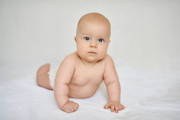 Charming baby on white background lying on his stomach, leaning on his hands with interest looks at camera. - 写真・画像