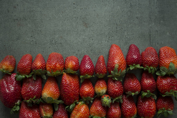 Frische saftige Erdbeeren in einer Reihe vor dunkelgrauem Hintergrund. Kopierraum.  - Foto, Bild
