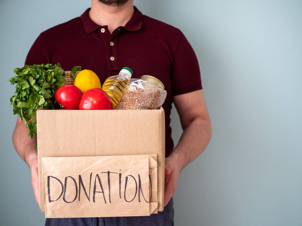 Homem mantém caixa de doação com bens em suas mãos, conceito de ajuda de vizinhança
 - Foto, Imagem