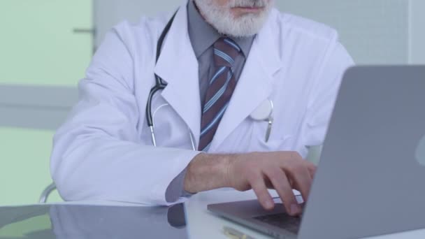 Surgeon looking at x-ray image, typing on laptop, entering results of analysis - Filmati, video
