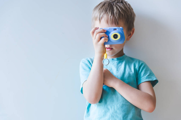 szőke kisfiú fényképezőgéppel a kezében és fényképezés otthon - Fotó, kép