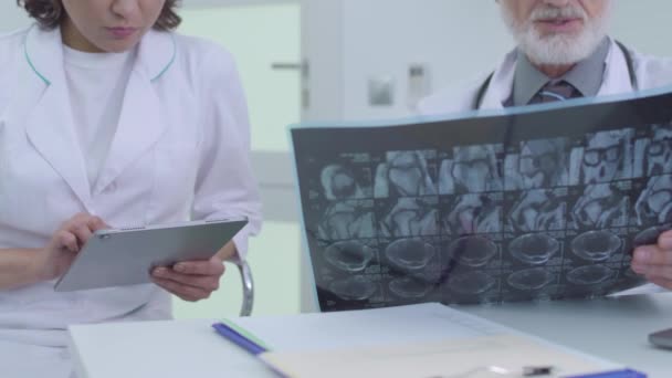 Nurse typing on tablet, listening to senior doctor, analyzing tomographic image - Felvétel, videó