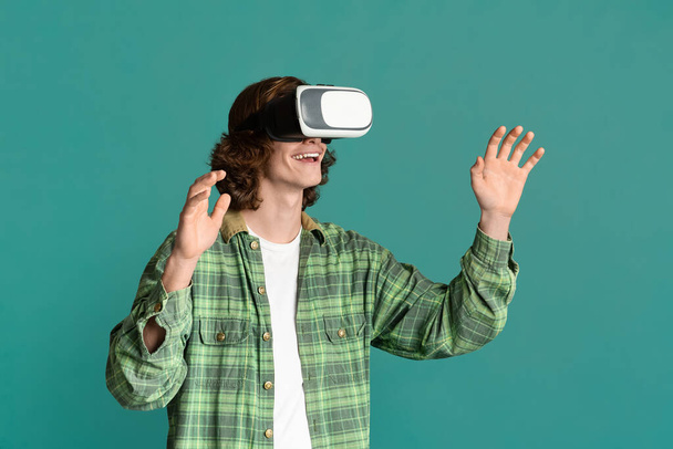 Du divertissement moderne. Millennial guy en réalité virtuelle casque jouer à des jeux vidéo sur fond turquoise
 - Photo, image