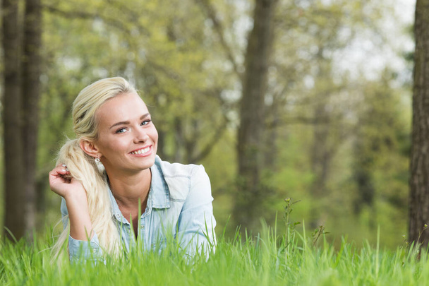 Happy smiling young woman laying on the green grass - 写真・画像