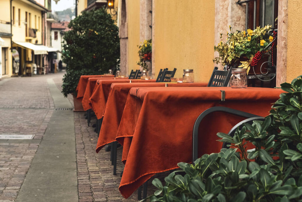 Mesas vacías de un café callejero en una calle desierta en Italia
. - Foto, Imagen