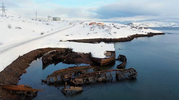 Vista aérea de la costa nevada del invierno con barcos en ruinas después del naufragio. Filmación. Antiguos barcos de pesca hundidos en la orilla del mar de Barents
. - Foto, imagen
