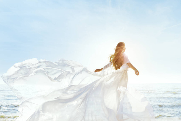 Donna sulla spiaggia soleggiata del mare in bianco Fluttering Dress, Moda modello posteriore vista, Seta panno ondulato sul vento
 - Foto, immagini