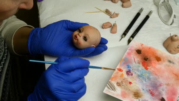 Puppenherstellung. Meisterpuppe malt mit dünnem Pinsel Lippen von Rohlingen für Puppen. Konzept der Herstellung von handgefertigten Puppen. - Filmmaterial, Video