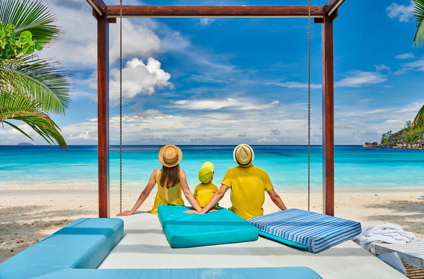 Family on beautiful Petite Anse beach, young couple in yellow with three year old toddler boy. Summer vacation at Seychelles, Mahe. - Photo, Image