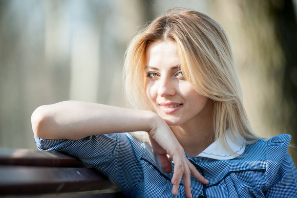 close up portrait of young blond woman sitting on bench on park background - Фото, изображение
