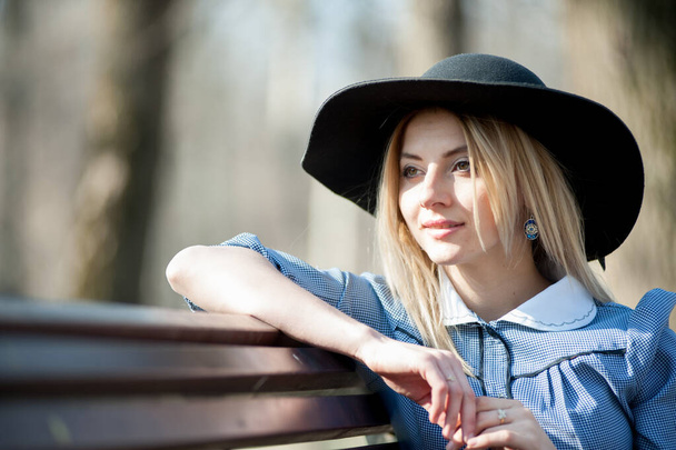 close up portrait of young blond woman sitting on bench on park background - Zdjęcie, obraz