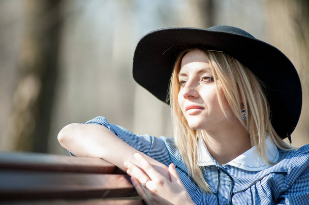 close up portrait of young blond woman sitting on bench on park background - Zdjęcie, obraz