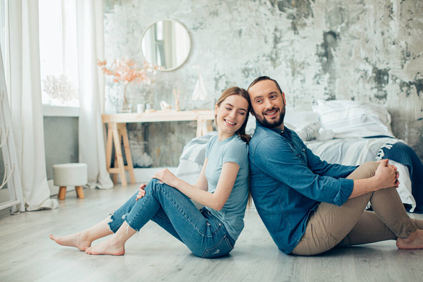 Cheerful young man and woman sitting barefooted in casual clothes at home and smiling stock photo - Photo, Image
