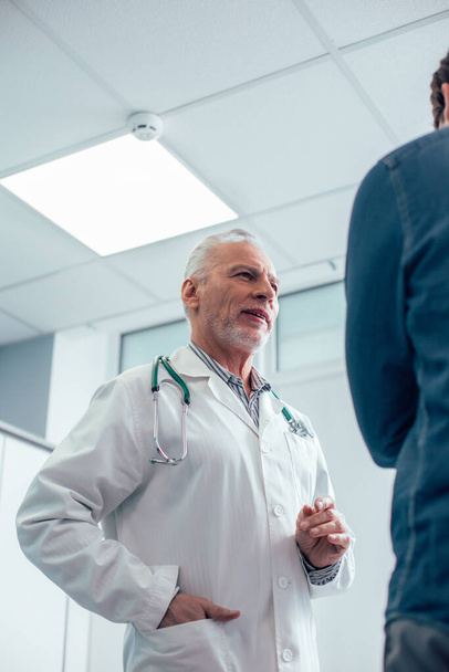 Calm mature doctor standing near the patient and having a calm talk stock photo - Фото, изображение