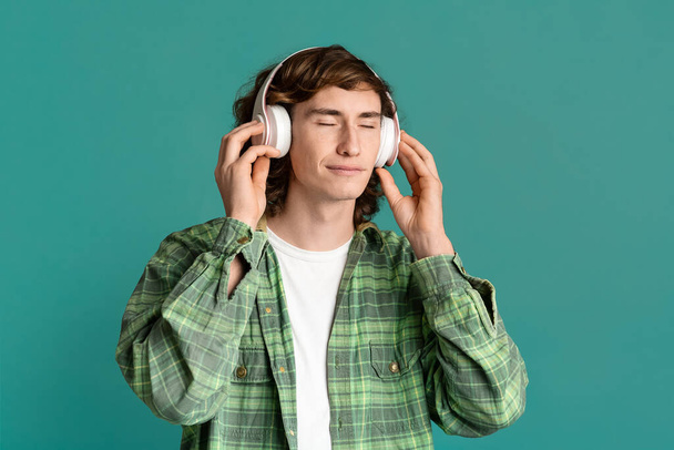 Chico joven pacífico en auriculares escuchando música con los ojos cerrados, fondo de color
 - Foto, imagen
