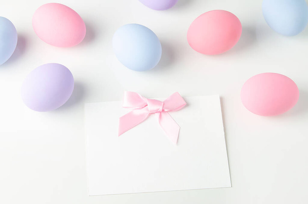 Blank white greeting card with pink ribbon bow and pastel easter eggs on white table background, Easter background - Фото, зображення