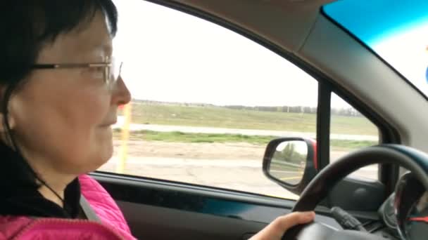Egy felnőtt nő szemüveggel, aki az autóját vezeti, úton van. Közelkép portré. - Felvétel, videó