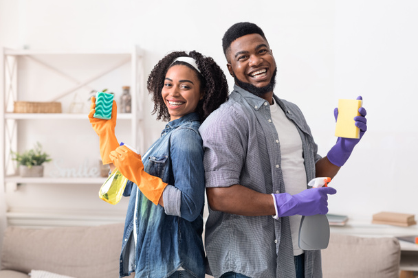 Birlikte ev işi yaparken temizlik malzemeleriyle poz veren neşeli afro çift. - Fotoğraf, Görsel
