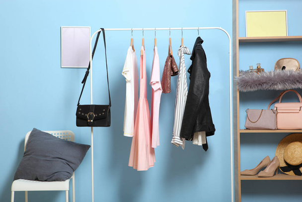 Fashionable clothes on hangers on a wardrobe rack in the background of the room. - Photo, Image