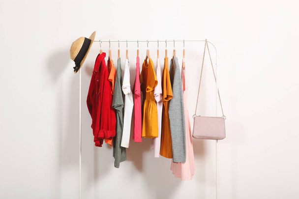 Fashionable clothes on hangers on a wardrobe rack on a light background. - Photo, Image