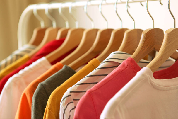 Μοντέρνα ρούχα σε κρεμάστρες σε ένα ράφι ντουλάπα στο παρασκήνιο του δωματίου. - Φωτογραφία, εικόνα