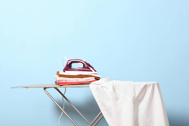 Iron and a stack of clothes on an ironing board on a colored background. - Photo, Image