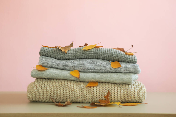 Een stapel warme truien en herfstbladeren op tafel. - Foto, afbeelding