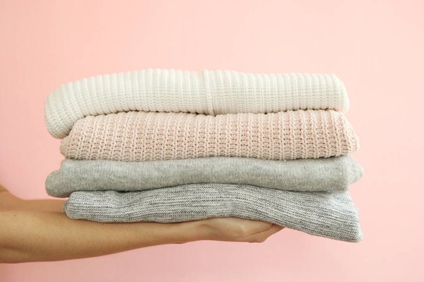 A stack of sweaters in female hands on a colored background. Warm clothes. - Foto, afbeelding
