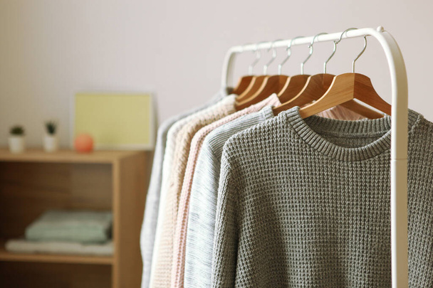 Warm sweaters on a wardrobe hanger on a light background. Autumn, winter clothes. - Zdjęcie, obraz
