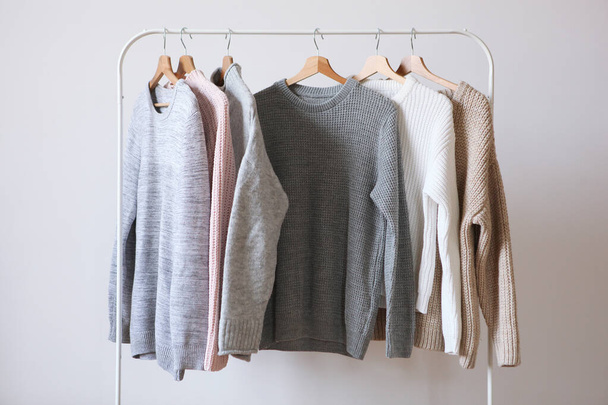 Теплые свитера на вешалке для гардероба на светлом фоне. Осень, зимняя одежда
. - Фото, изображение