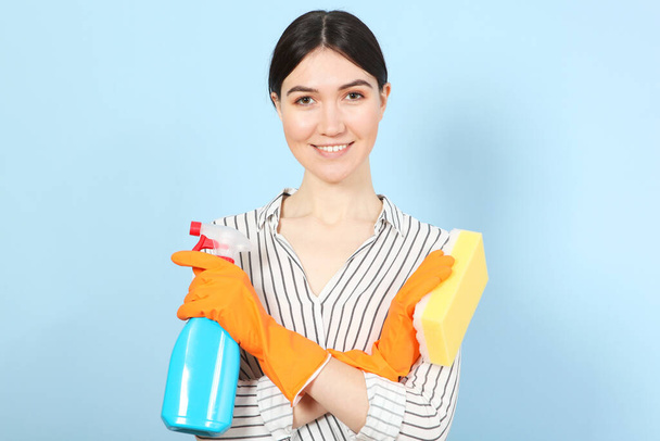 Молодая домохозяйка держит в руках чистящие средства на цветном фоне
. - Фото, изображение