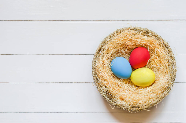 Colorful easter eggs at brown nest on white wooden table and blue background - Foto, Imagen