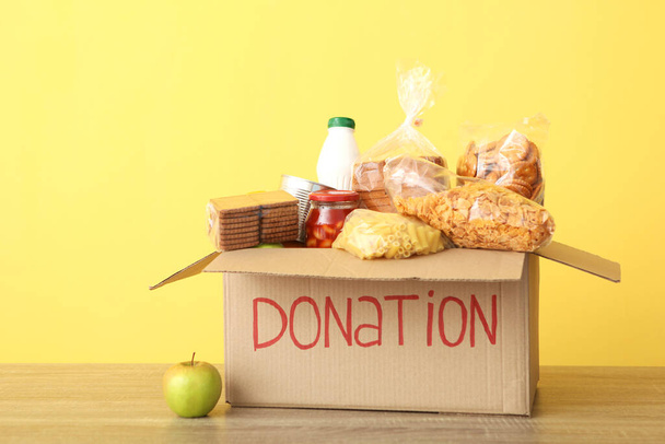Kisten mit Spenden mit den notwendigen Dingen auf dem Tisch vor farbigem Hintergrund. Wohltätigkeit, Ehrenamt. - Foto, Bild