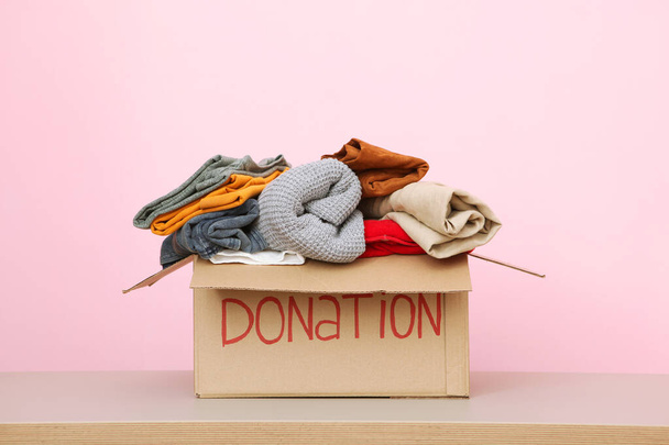 Kisten mit Spenden mit den notwendigen Dingen auf dem Tisch vor farbigem Hintergrund. Wohltätigkeit, Ehrenamt. - Foto, Bild