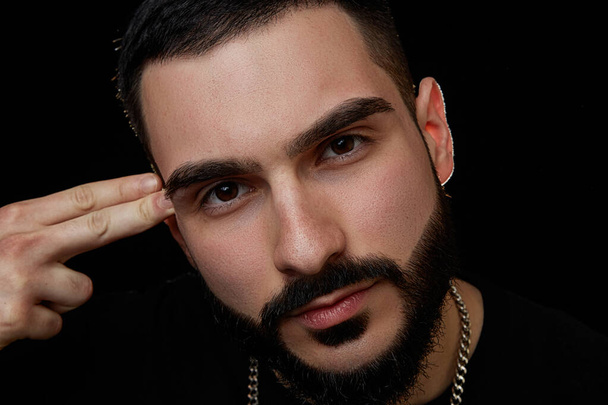 close-up of a dramatic portrait of a young serious guy, musician, singer, rapper with a beard in black clothes on a black isolated background. - Fotoğraf, Görsel