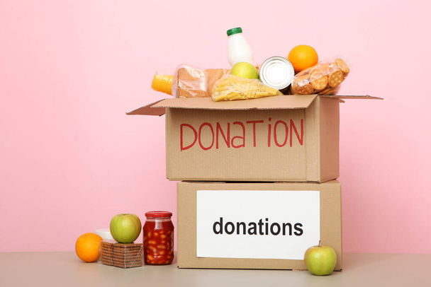 dozen met donaties met de nodige dingen op de tafel op een gekleurde achtergrond. Liefdadigheid, vrijwilligerswerk. - Foto, afbeelding