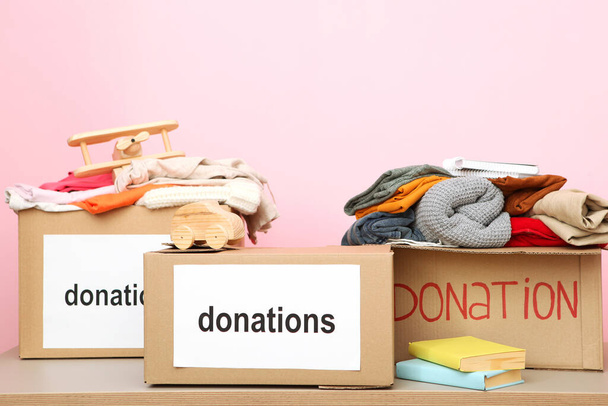 коробки с пожертвованиями с необходимыми вещами на столе на цветном фоне. Благотворительность, волонтерство
. - Фото, изображение